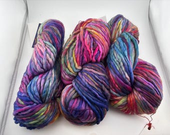 May include: Three skeins of thick, chunky yarn featuring a variegated color palette of vibrant pink, deep purple, bright blue, and sunny yellow. The yarn has a soft, twisted texture and is presented in a loose, bundled formation.