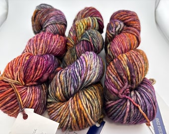 May include: Three skeins of thick, hand-dyed yarn featuring a variegated color palette of deep purple, vibrant orange, golden yellow, and hints of dark charcoal gray. Each skein is twisted into a bundle and includes a white paper product tag.