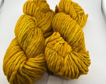 Puede incluir: Cuatro madejas de hilo grueso de color amarillo mostaza dispuestas en un grupo. El hilo presenta una textura trenzada pesada con un tono amarillo dorado consistente en cada madeja, mostrando una apariencia suave y voluminosa para tejer.