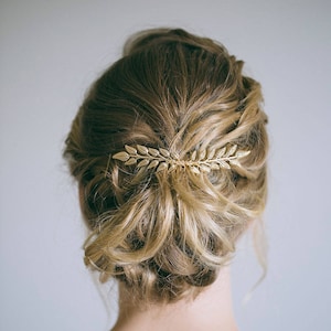 May include: A woman with blonde hair wearing a white lace dress with a gold leaf hair comb in her hair.