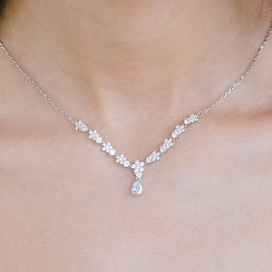 May include: A silver necklace with a teardrop-shaped pendant and a delicate floral design. The necklace is worn by a person with long dark hair.