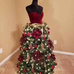 Op de afbeelding: Een kerstboom versierd met een rode fluwelen jurk, gouden ornamenten en rode en gouden bloemen.