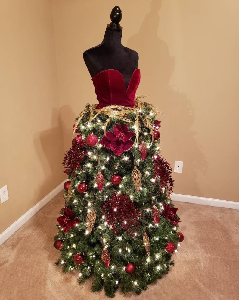 Op de afbeelding: Een kerstboom versierd met een rode fluwelen jurk, gouden ornamenten en rode en gouden bloemen.