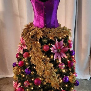 Op de afbeelding: Een paarse satijnen corset wordt gebruikt als basis voor een kerstboom die versierd is met roze en paarse kerstballen, gouden tinsel en roze kerststerren.
