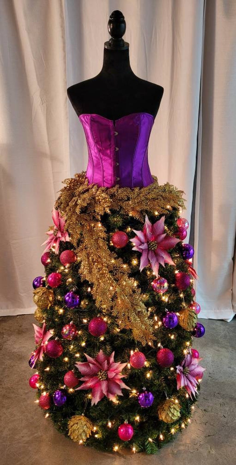 Op de afbeelding: Een paarse satijnen corset wordt gebruikt als basis voor een kerstboom die versierd is met roze en paarse kerstballen, gouden tinsel en roze kerststerren.