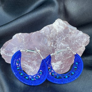 May include: A pair of blue crocheted hoop earrings with silver clasps and blue crystal accents.