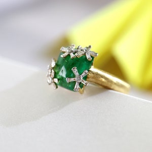 Puede incluir: Un anillo de oro con una gran esmeralda verde rodeada de pequeños diamantes engastados en forma de estrella.