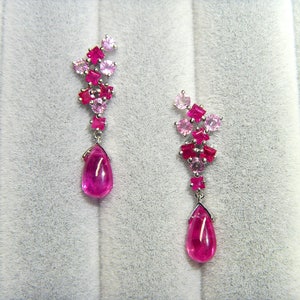 May include: A pair of pink and red gemstone earrings with teardrop-shaped pink gemstones hanging from a cluster of smaller square-shaped gemstones.
