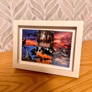 May include: A white picture frame with a collage of six square photos. The photos are of various landscapes, including a sunset, a forest, and a beach. The frame is on a wooden surface.