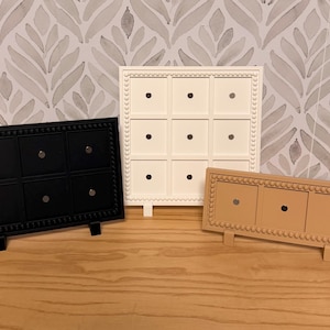 May include: Three decorative wooden boxes in black, white, and tan. The black box has six squares, the white box has nine, and the tan box has three. Each box has a beaded border and small silver knobs.