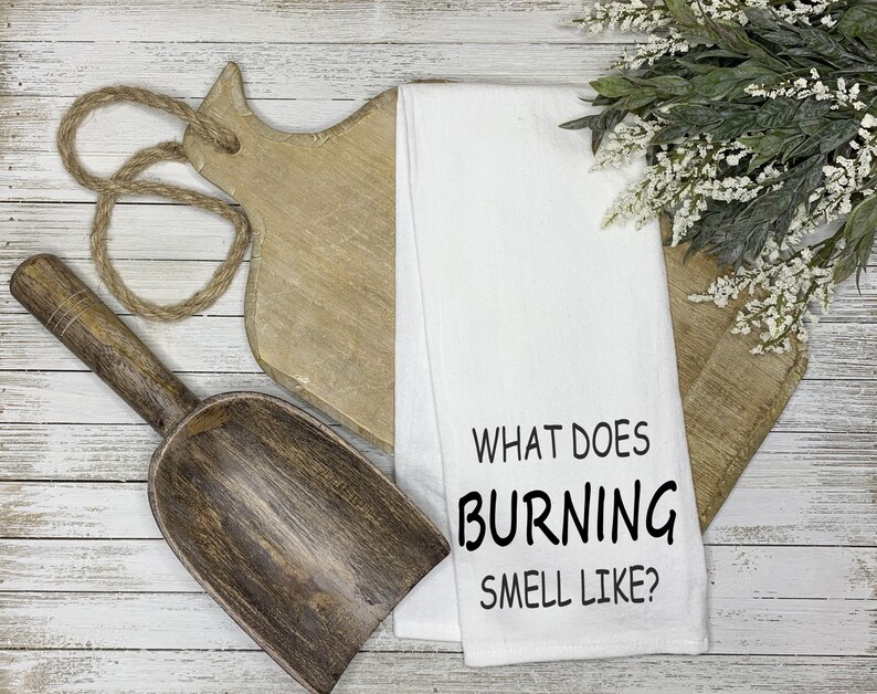 Puede incluir: Toalla de cocina blanca con texto negro que dice "What does burning smell like?"