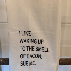 May include: White kitchen towel with black text that reads "I like waking up to the smell of bacon. Sue me."