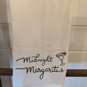 May include: White kitchen towel with black text that reads "Midnight Margaritas" and a black silhouette of a margarita glass with a lime wedge.
