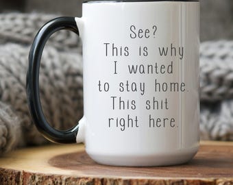 Könnte beinhalten: Weißer Keramikbecher mit schwarzem Henkel und Rand. Der Becher trägt den Text "See? This is why I wanted to stay home. This shit right here." in Schwarz. Der Becher steht auf einer Holzoberfläche.