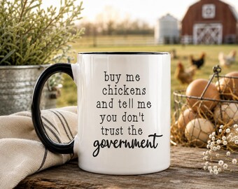 Könnte beinhalten: Ein weißer Keramikbecher mit schwarzem Henkel und schwarzem Innenrand. Auf der Vorderseite des Bechers steht in schwarzer Schrift: buy me chickens and tell me you don't trust the government. Der Becher hat eine glatte Oberfläche und eine zylindrische Form.