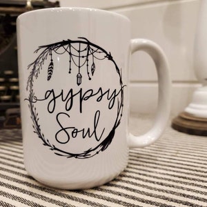 May include: White ceramic mug with a black design of a dreamcatcher with feathers and the text "gypsy soul".