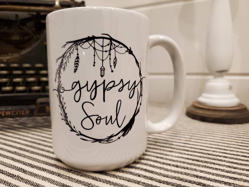 May include: White ceramic mug with a black design of a dreamcatcher with feathers and the text "gypsy soul".