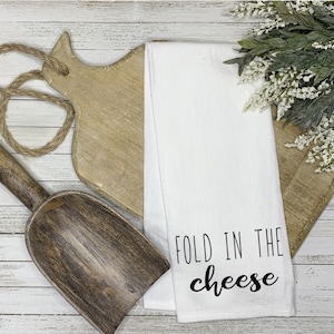 May include: White kitchen towel with the text "Fold in the cheese" in black lettering.
