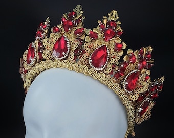 May include: A gold crown with red gemstone accents. The crown is on a white mannequin head.