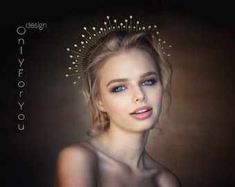 May include: A woman with blonde hair is wearing a gold crown with white pearls. The crown has a starburst design. The woman is looking at the camera and has a neutral expression. The background is dark.