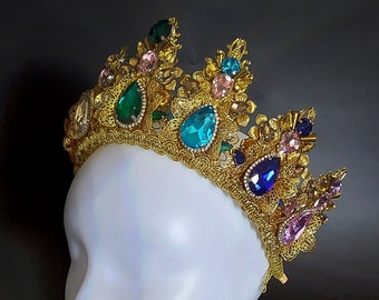 May include: A gold crown with colorful gemstones, including pink, blue, green, and teal, on a white mannequin head.