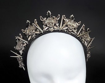 May include: A black headband with silver skull and sword accents. The headband is decorated with multiple silver spikes.