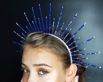 May include: A blue beaded crown with a silver band. The crown is shaped like a sun with rays extending out from the center.