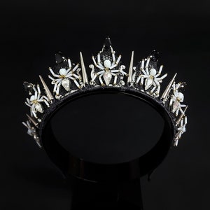 May include: A black crown with silver spikes and white spider embellishments.