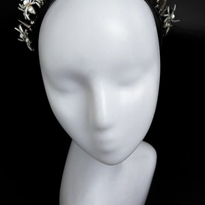 May include: A black headband with silver spikes and white spider embellishments. The headband is on a white mannequin head.