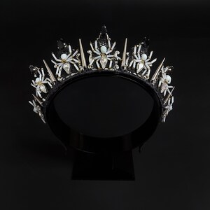 May include: Black crown with silver spikes and white spider embellishments. The crown is made of fabric and has a black velvet band.