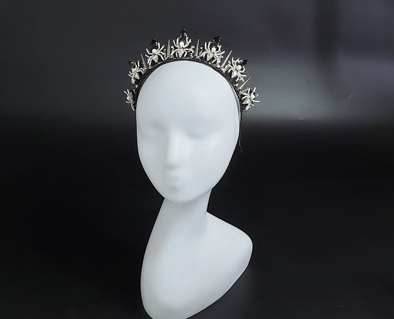 May include: A black headband with a silver crown of spiders. The spiders have white pearl accents.