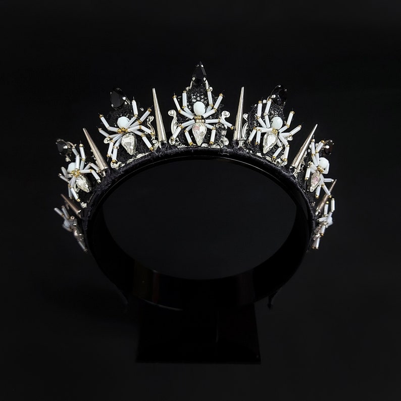 May include: A black crown with silver spikes and white spider embellishments.