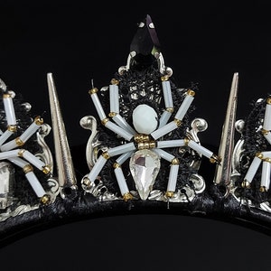 May include: A black headband with silver spikes and white spider accents. The headband is decorated with black lace, white beads, and rhinestones.