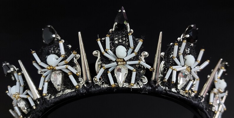 May include: A black headband with silver spikes and white spider accents. The headband is decorated with black lace, white beads, and rhinestones.