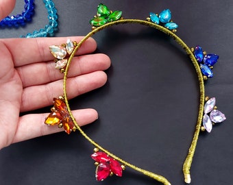 May include: A gold headband with colorful rhinestones in a rainbow pattern. The headband is decorated with clusters of rhinestones in shades of green, blue, orange, red, and pink.