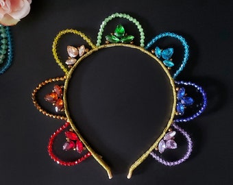 May include: A rainbow-colored beaded headband with a gold base and crystal accents. Each section of the headband is a different color of the rainbow, with a crystal cluster in the center of each section.