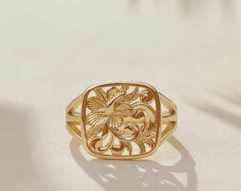 May include: A gold ring featuring a square-shaped face with an openwork design. The center displays a detailed hibiscus flower surrounded by swirling scrollwork patterns. The band is split into two thin, polished gold segments on each side.