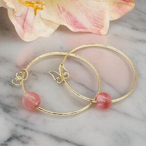 May include: Two gold bangle bracelets with pink glass beads. Each bracelet has a delicate butterfly charm.