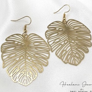 May include: Gold-tone earrings featuring a delicate, cutout design of a monstera leaf.
