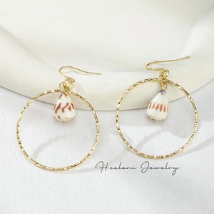 May include: Gold hoop earrings with a small white seashell charm hanging from each hoop. The earrings are on a white background.  Healanni Jewelry.