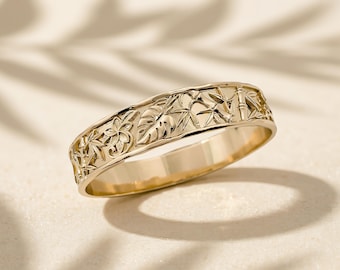 Op de afbeelding: Een gouden ring met een reliëfpatroon van tropische flora, waaronder monstera-bladeren, plumeria-bloemen en bamboestengels. Het metaal heeft een gepolijste, reflecterende afwerking met verdiepte details die het botanische ontwerp benadrukken.
