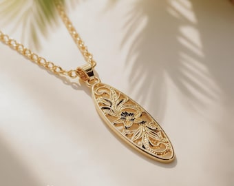 Op de afbeelding: Een goudkleurige ketting met een langwerpig ovaal hangertje met een opengewerkt bloemmotief. De hanger hangt aan een bijpassende goudkleurige ketting. Het metalen oppervlak toont ingewikkelde uitgesneden blad- en bloempatronen.