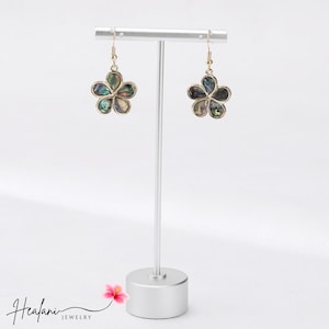 May include: Gold-coloured flower-shaped earrings with iridescent abalone shell petals. The earrings are displayed on a silver jewellery stand against a white background. The brand name "Healani Jewelry" is visible.