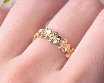 May include: A gold-toned ring featuring a continuous band of small, polished five-petaled flowers. The metal surface is smooth and reflective, creating a repeating floral pattern that encircles the finger with a bright, metallic finish.