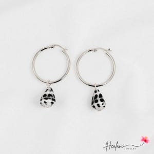 May include: Two silver hoop earrings, each with a teardrop-shaped pendant. The pendants are white with black spots, creating a Dalmatian-like pattern. The earrings are set against a white backdrop. The word "Healani" is written in cursive.