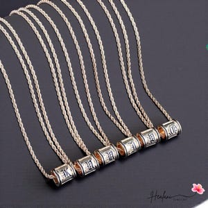 May include: Silver-coloured rope chain necklaces with cylindrical pendants. Each pendant features a different letter in a black, stylised font. The necklaces are displayed on a black surface. The brand name "Heafani Jewelry" is visible in the bottom right corner.