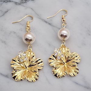 May include: Gold tone earrings with a pearl and a gold hibiscus flower with rhinestones.