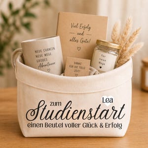 Könnte beinhalten: Ein cremefarbener Stoffkorb mit der Aufschrift "zum Studienstart einen Beutel voller Glück & Erfolg" und dem Namen "Lea". Darin befinden sich eine beige Tasse, ein braunes Notizbuch, ein kleines Glas mit Kerze und eine Karte "DANKE FÜR DIE TOLLE ZEIT!"