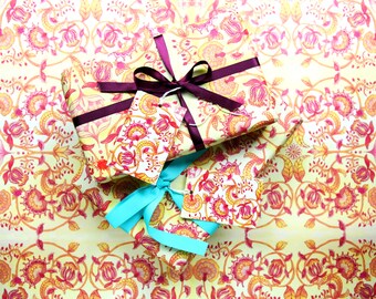 Peut inclure: Deux cadeaux emballés dans du papier à motifs jaunes avec des motifs floraux rouges et orange. Les cadeaux sont attachés avec des rubans violets et turquoise et ont des étiquettes cadeaux assorties.