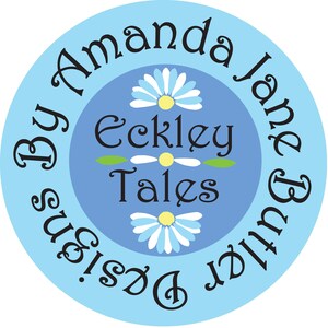 K&ouml;nnte beinhalten: Ein blauer Kreis mit wei&szlig;em Text, der "By Amanda Jane & Butter Designs." lautet. Im Inneren des Kreises befindet sich ein kleinerer Kreis mit dem Text "Eckley Tales" und drei wei&szlig;en G&auml;nsebl&uuml;mchen mit gelben Zentren.